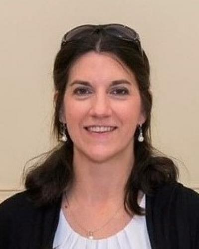 A smiling woman with long dark hair wearing a black cardigan and a white top.